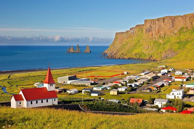 The red-roofed church above Vík with the Reynisdrangar sea stacks out at sea
