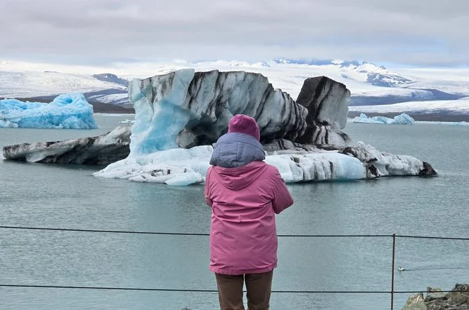 A visitor in a pink jacket looking at icebergs floating in the Jökulsárlón lagoon