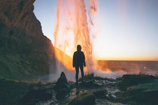 A silhouetted person behind Seljalandsfoss with low sun glowing through the falling water