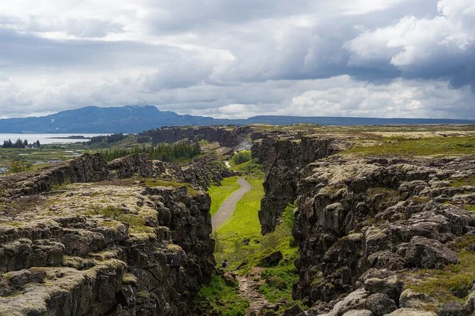 A path running along a rocky rift valley at Þingvellir under a cloudy sky